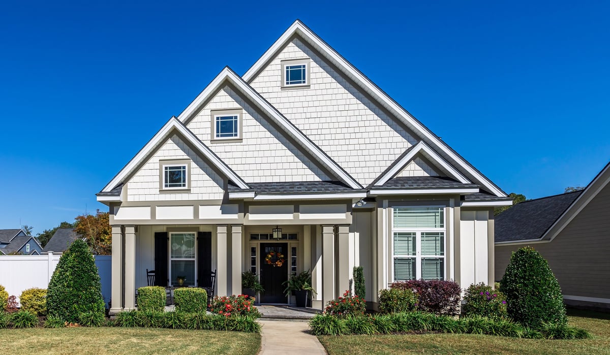 Front view of a new construction craftsman style white house with a triple pitched roof and landscaping