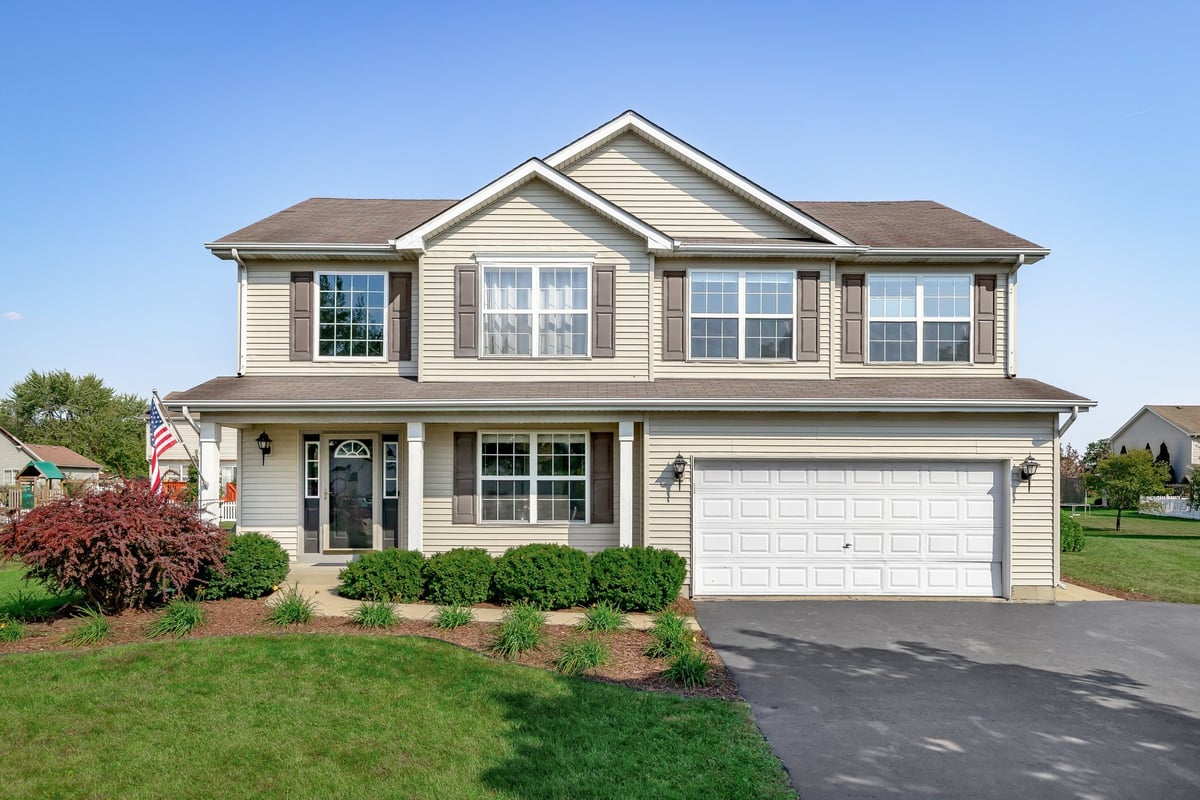 A new suburban house with tan siding, brown window shutters, and a front porch