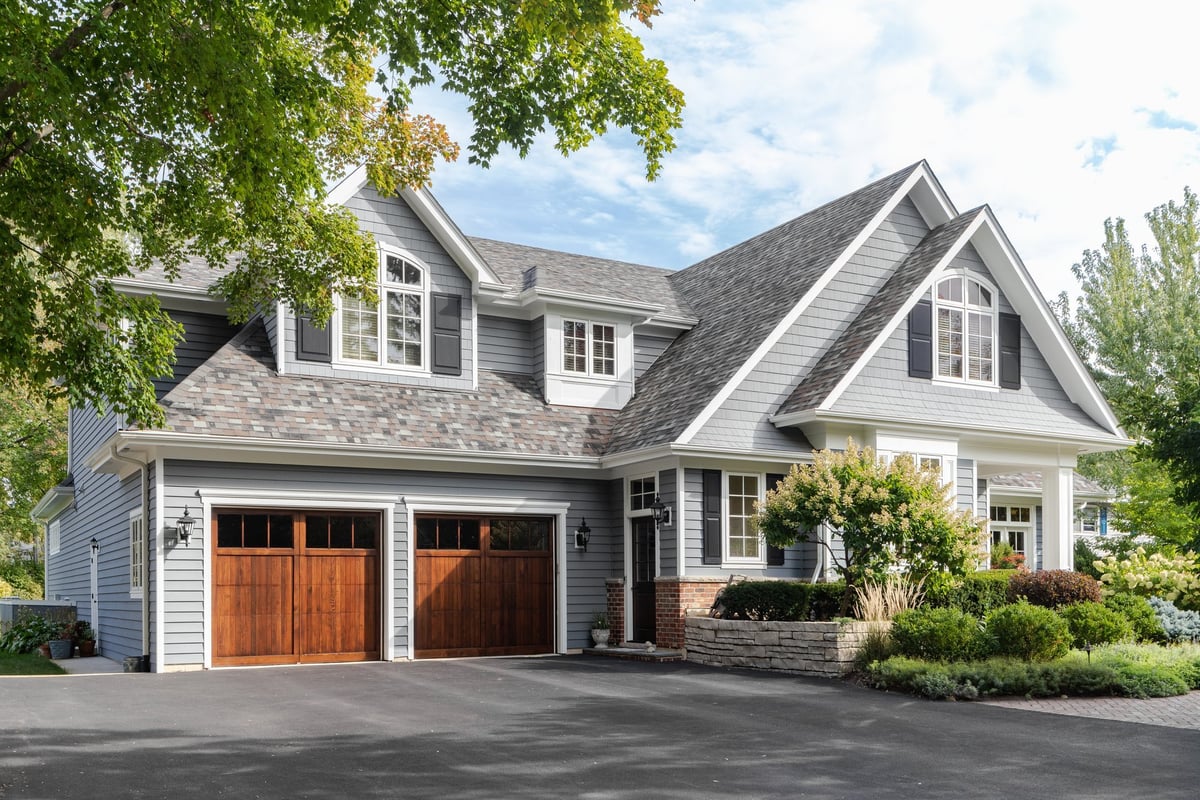 Large grey and white modern farmhouse with two wooden garage doors and beautiful landscaping