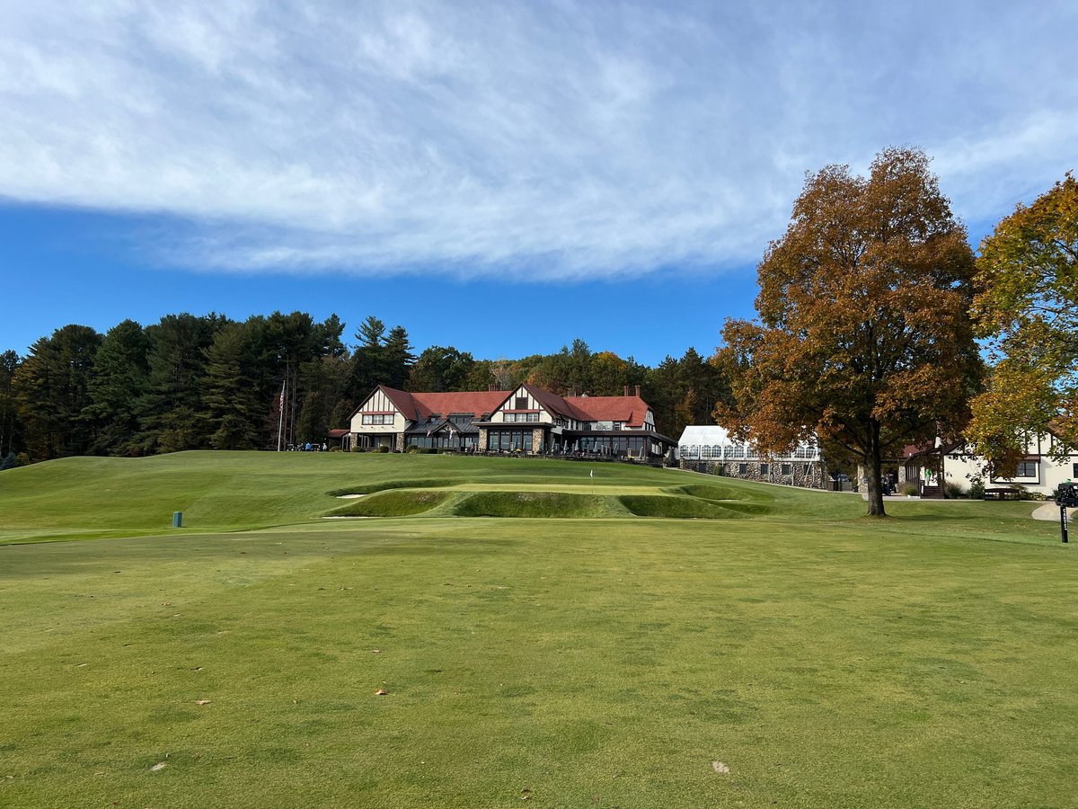 A scenic view of a golf course with a clubhouse in the background, surrounded by trees under a clear blue sky