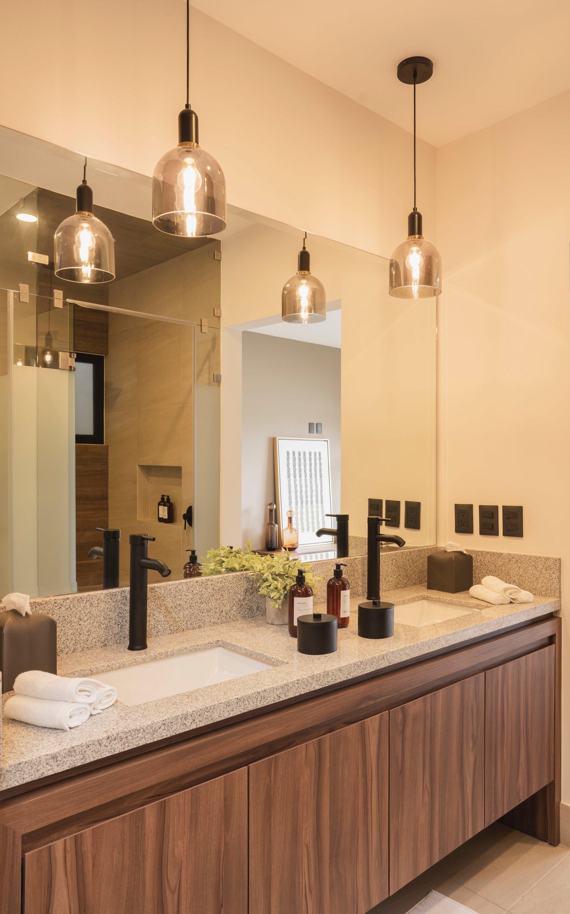 Modern bathroom with double vanity, stone countertop, wood cabinetry, black fixtures, and glass pendant lights
