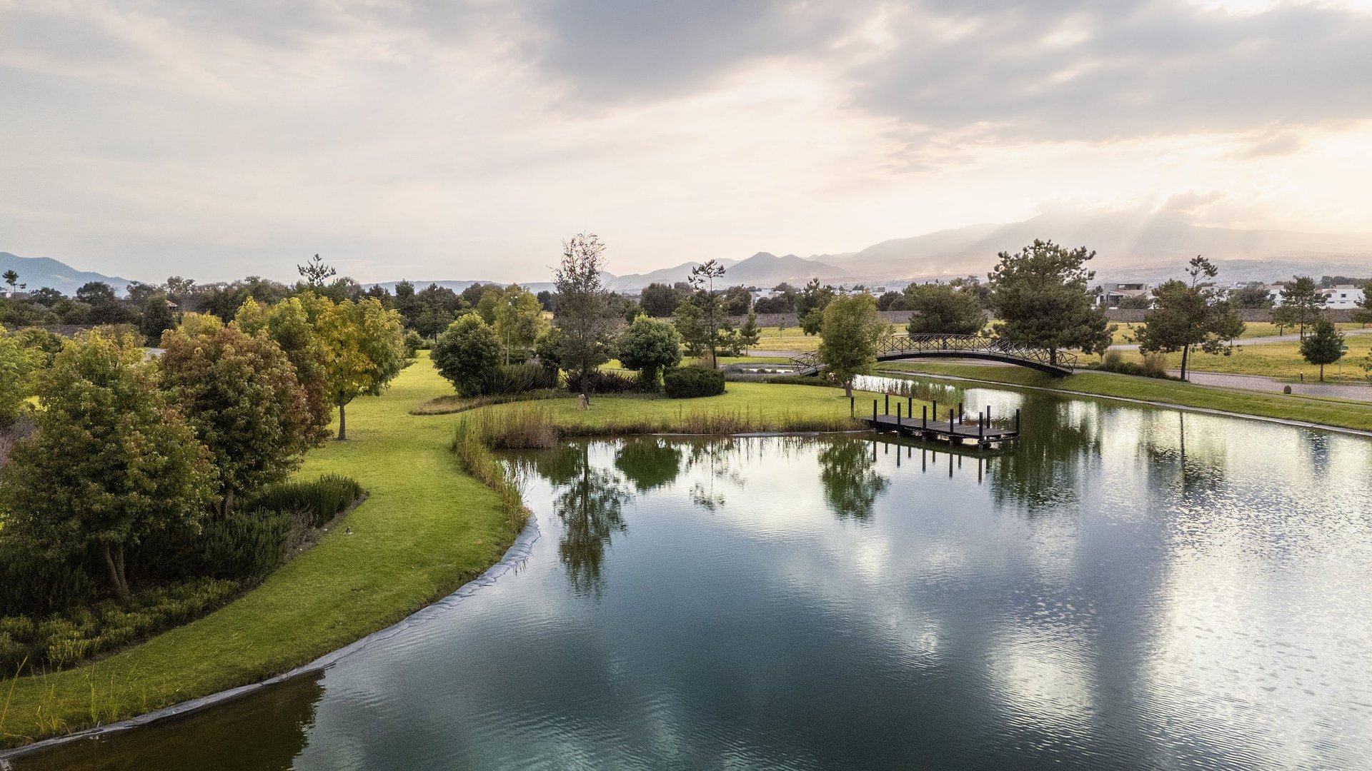 Peaceful river landscape with green meadows, scattered trees, and cloudy sky reflecting in calm water