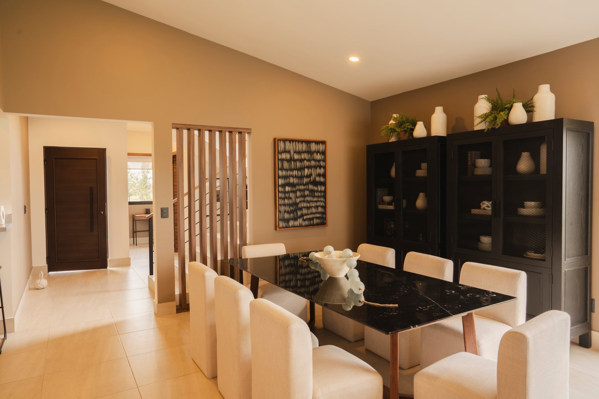 Modern dining room with black table, beige chairs, orange walls, and black shelving unit displaying decorative items