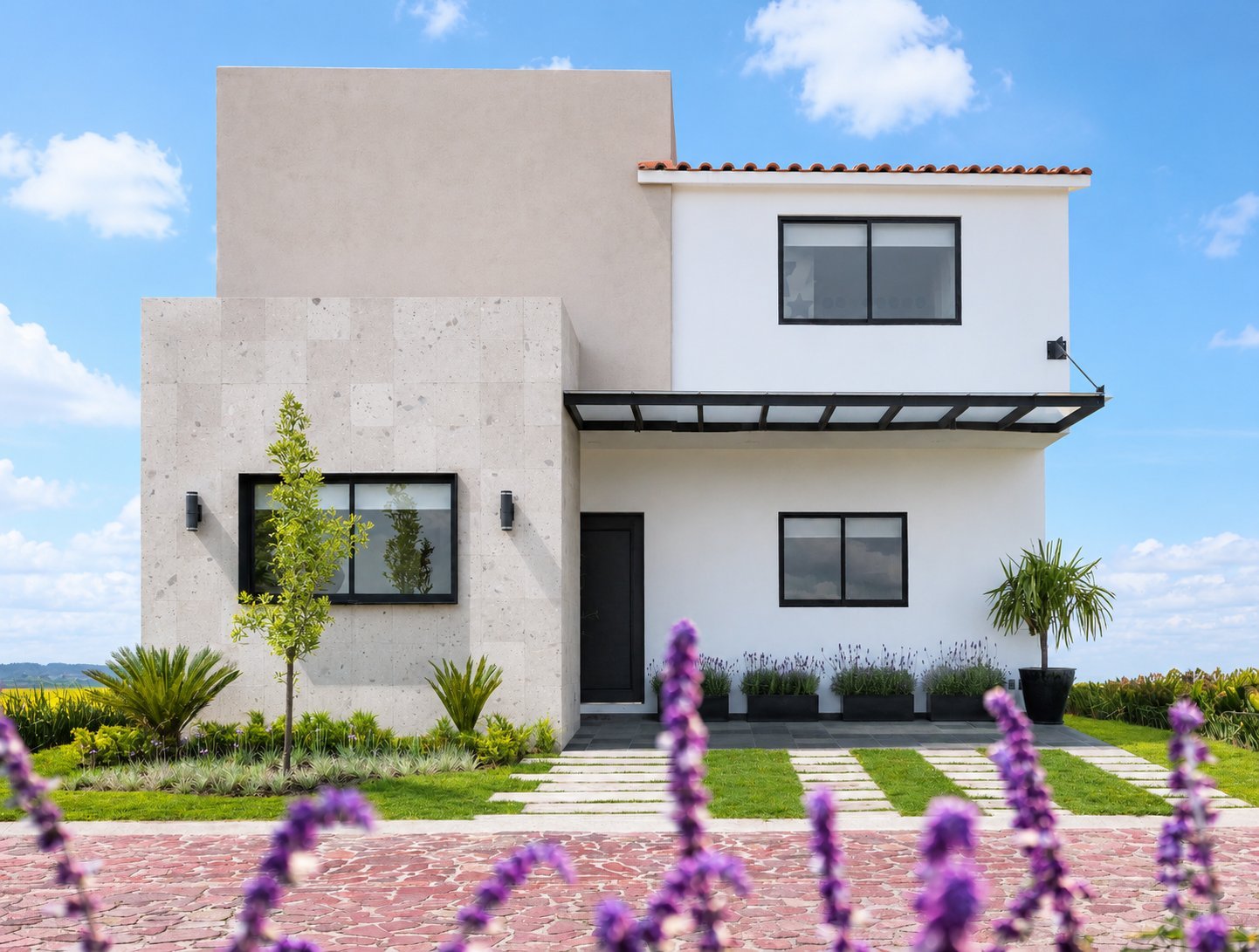 Modern white and beige house with geometric architecture, large windows, and purple flowers in the foreground under blue sky