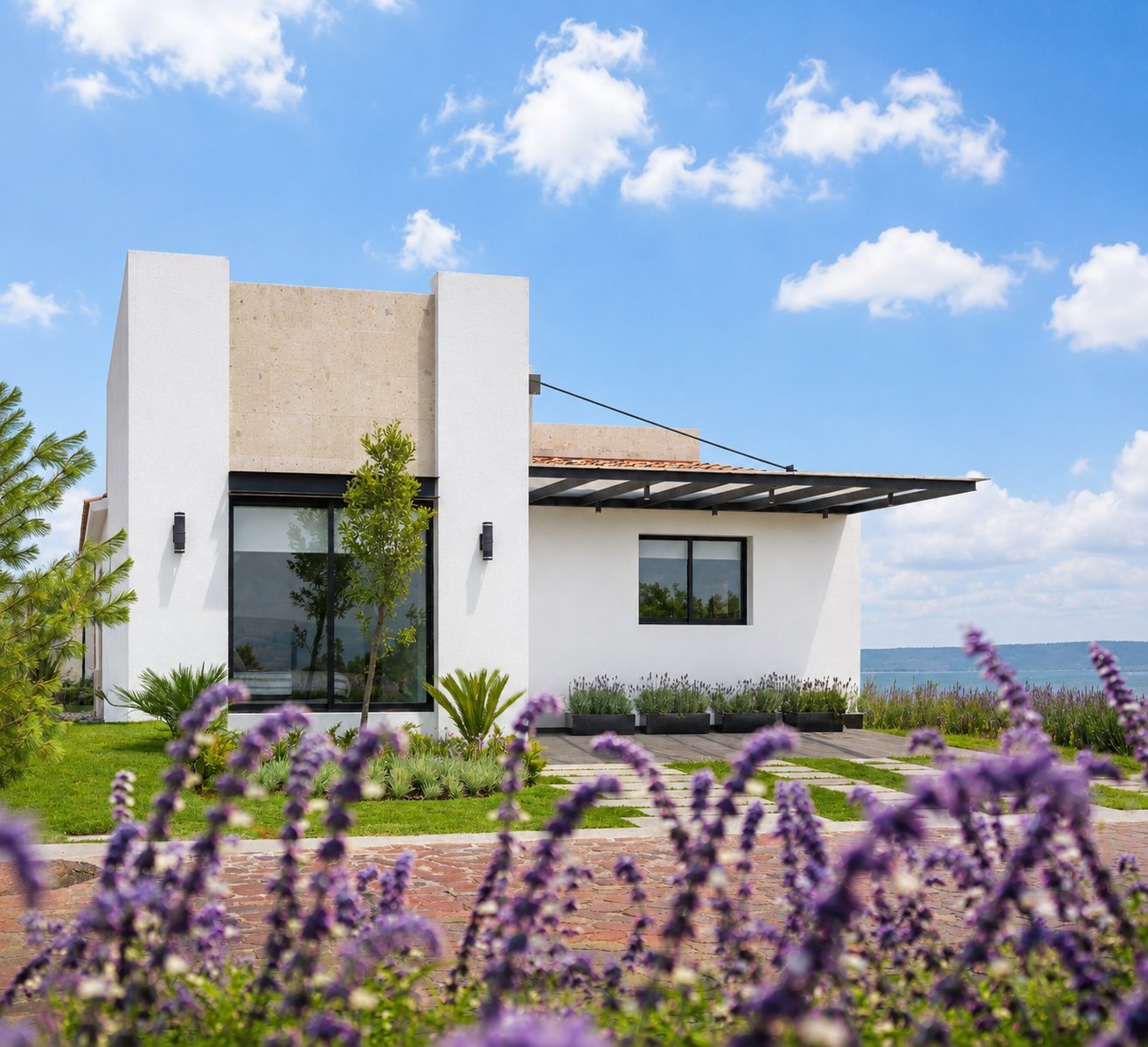 Modern white house with metal pergola surrounded by purple lavender flowers and green landscaping on a sunny day
