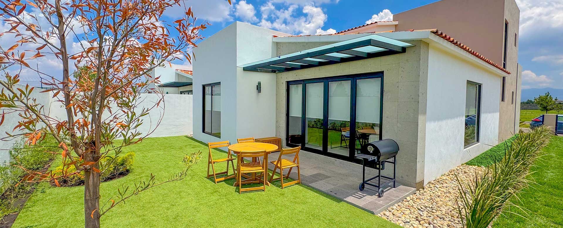 Modern white house with green roof overhang, patio seating, and manicured lawn