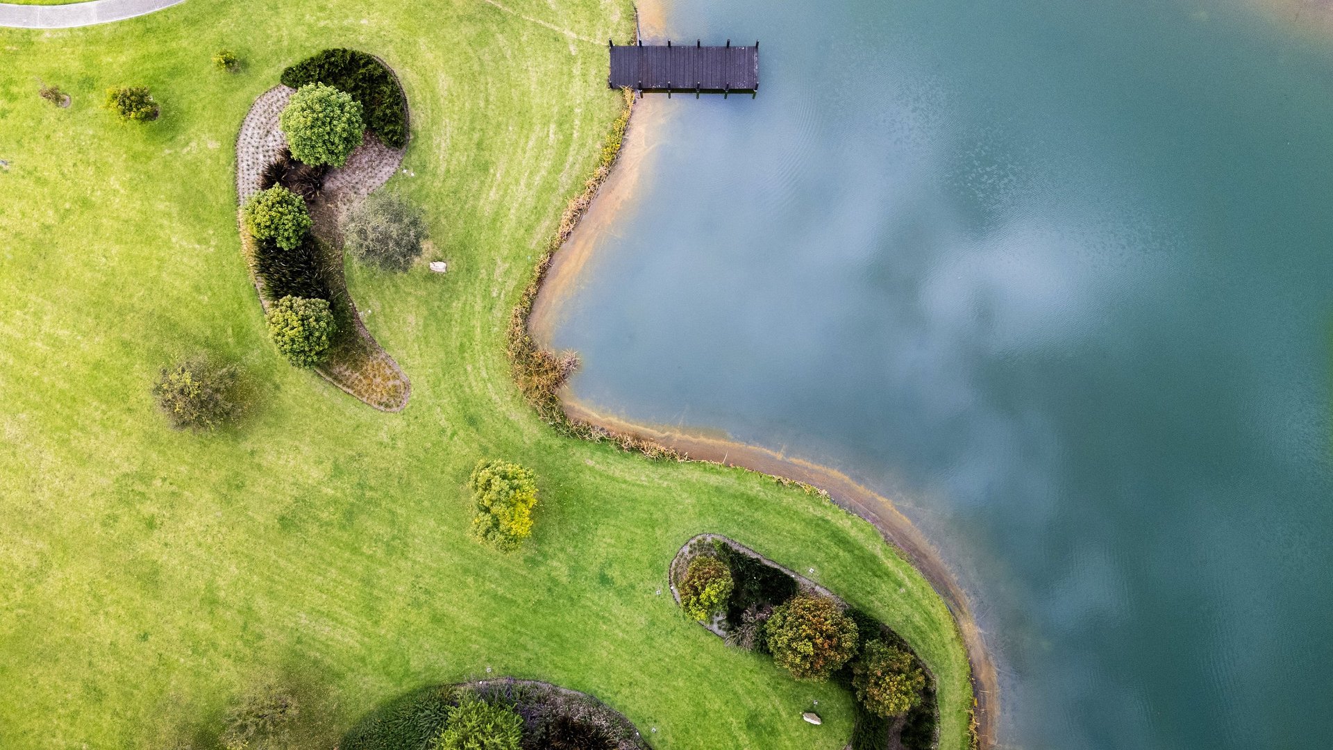 Aerial view of a verdant coastal peninsula with forested areas and a small dock extending into turquoise water