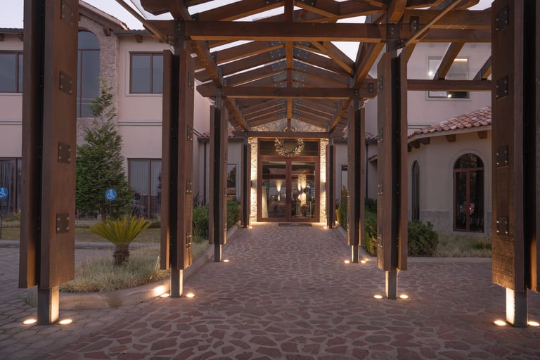 Modern covered walkway with wooden pergola structure, ambient ground lighting, brick paving, and surrounding residential buildings