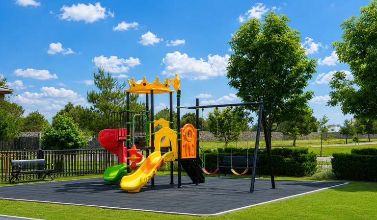 Colorful playground equipment with slides and climbing structures on black rubber surface in a sunny park setting surrounded by green trees and grass