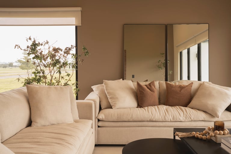 Modern living room with beige sectional sofa, decorative pillows, large window overlooking landscape, and minimalist decor
