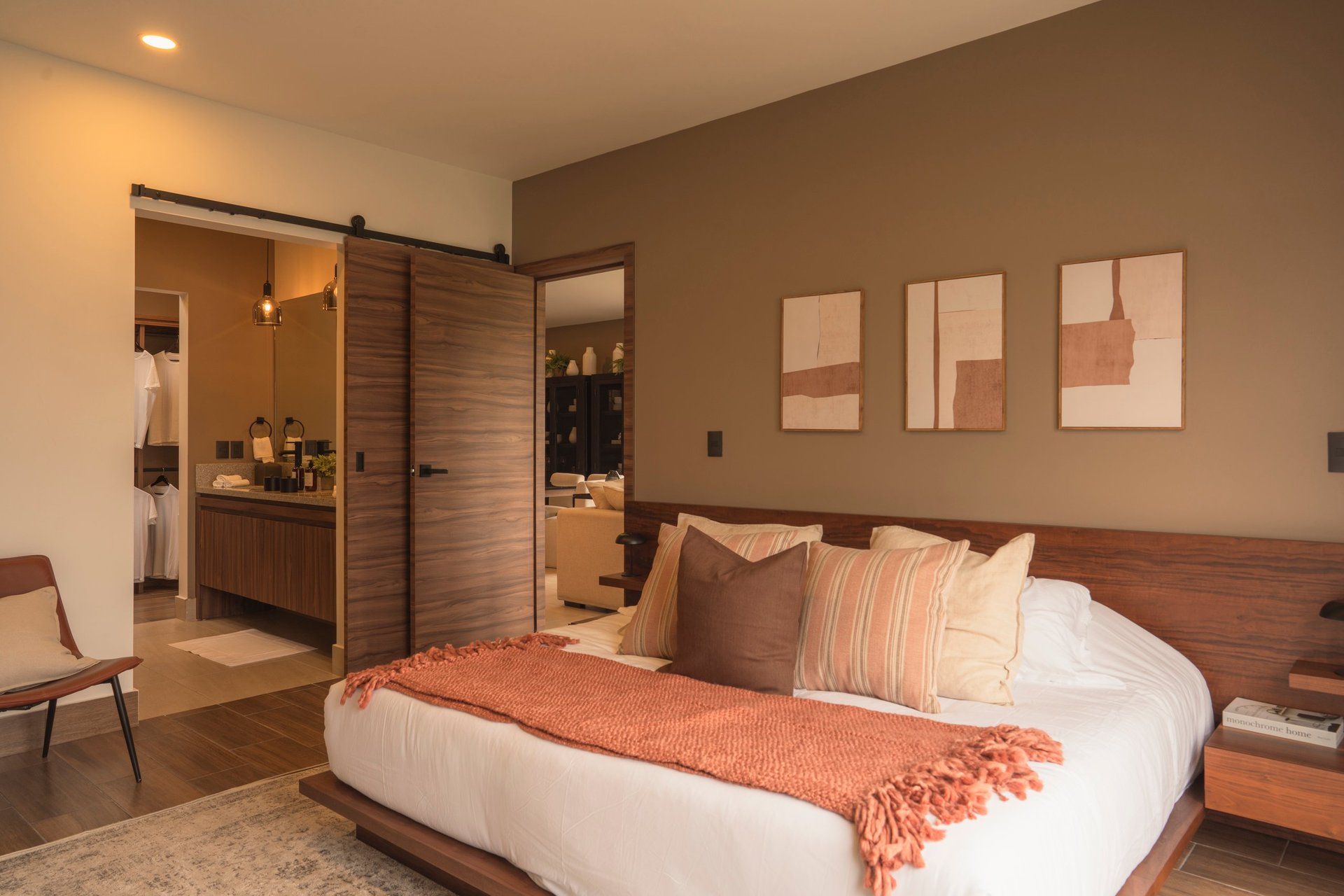 Modern bedroom with white bed, orange throw blanket, brown nightstands, and wooden sliding closet doors opening to ensuite bathroom