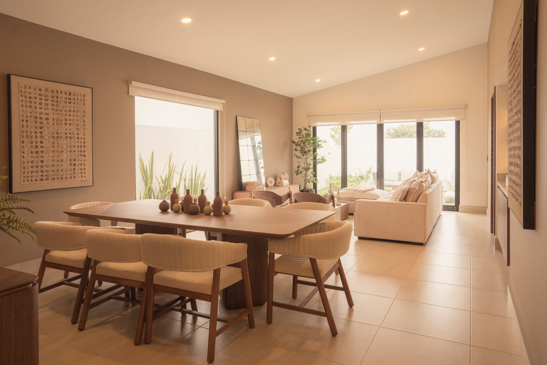Modern dining room with wooden table, beige chairs, large windows, and neutral earth-tone walls with recessed lighting